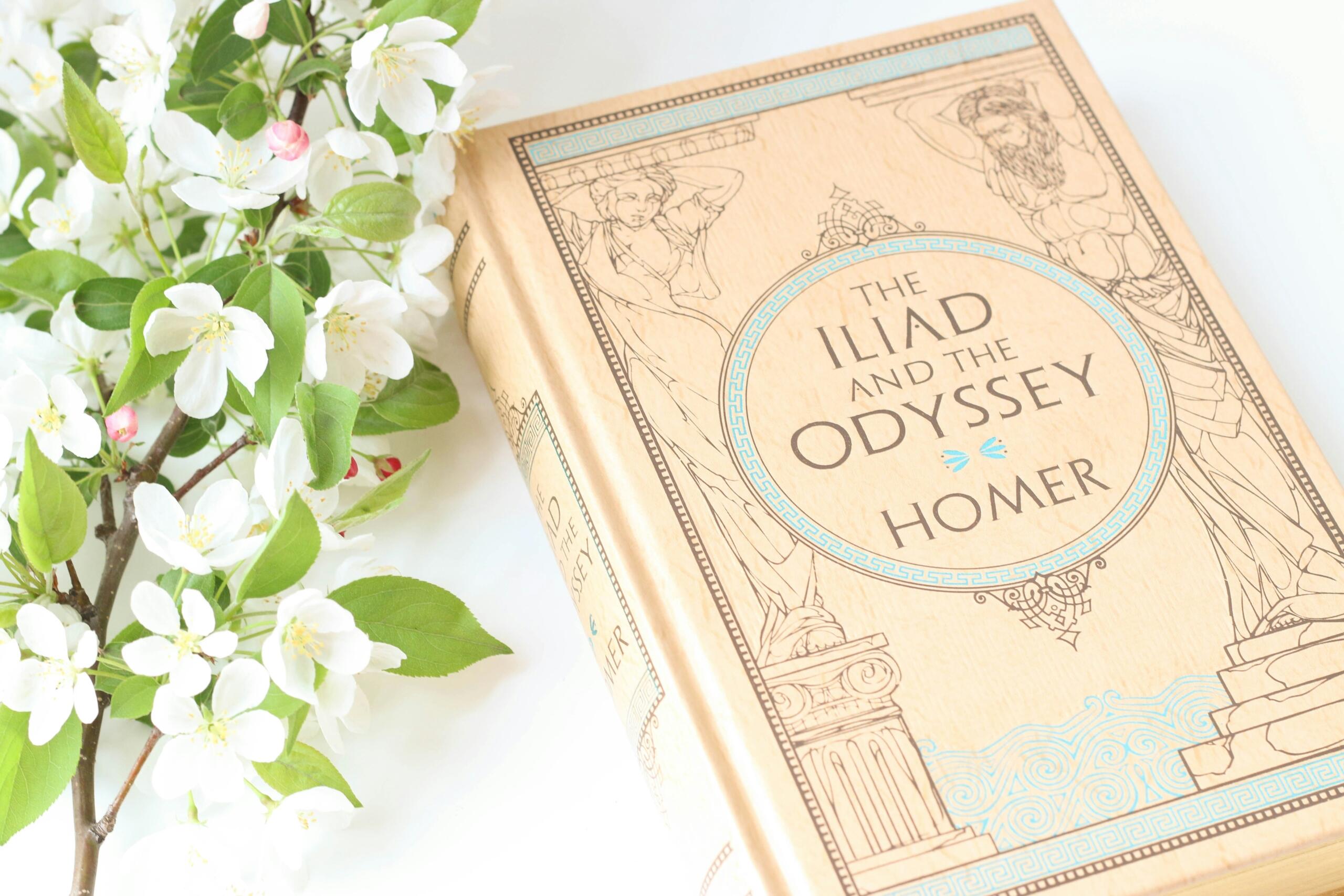 raamatu „The Iliad and the Odyssey” kaas valgel taustal õunapuuõite kõrval