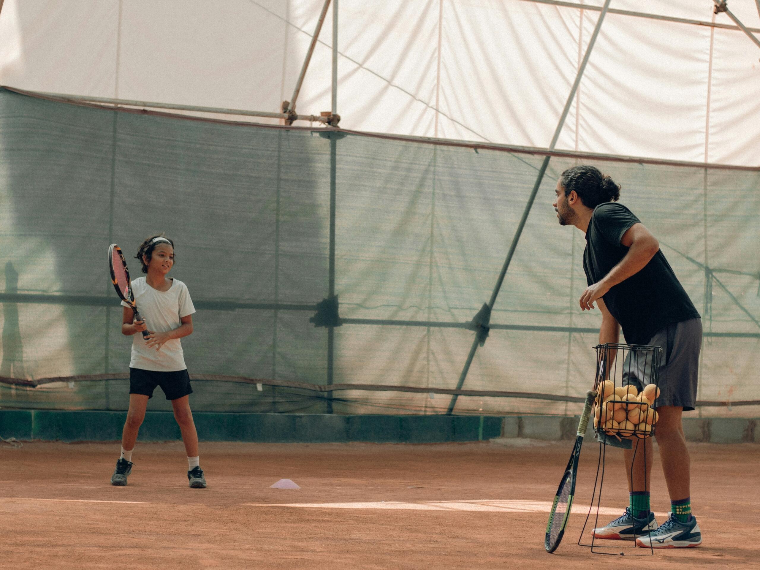 Tenniseetreener juhendab saviliivaväljakul noort õppijat treeningu ajal