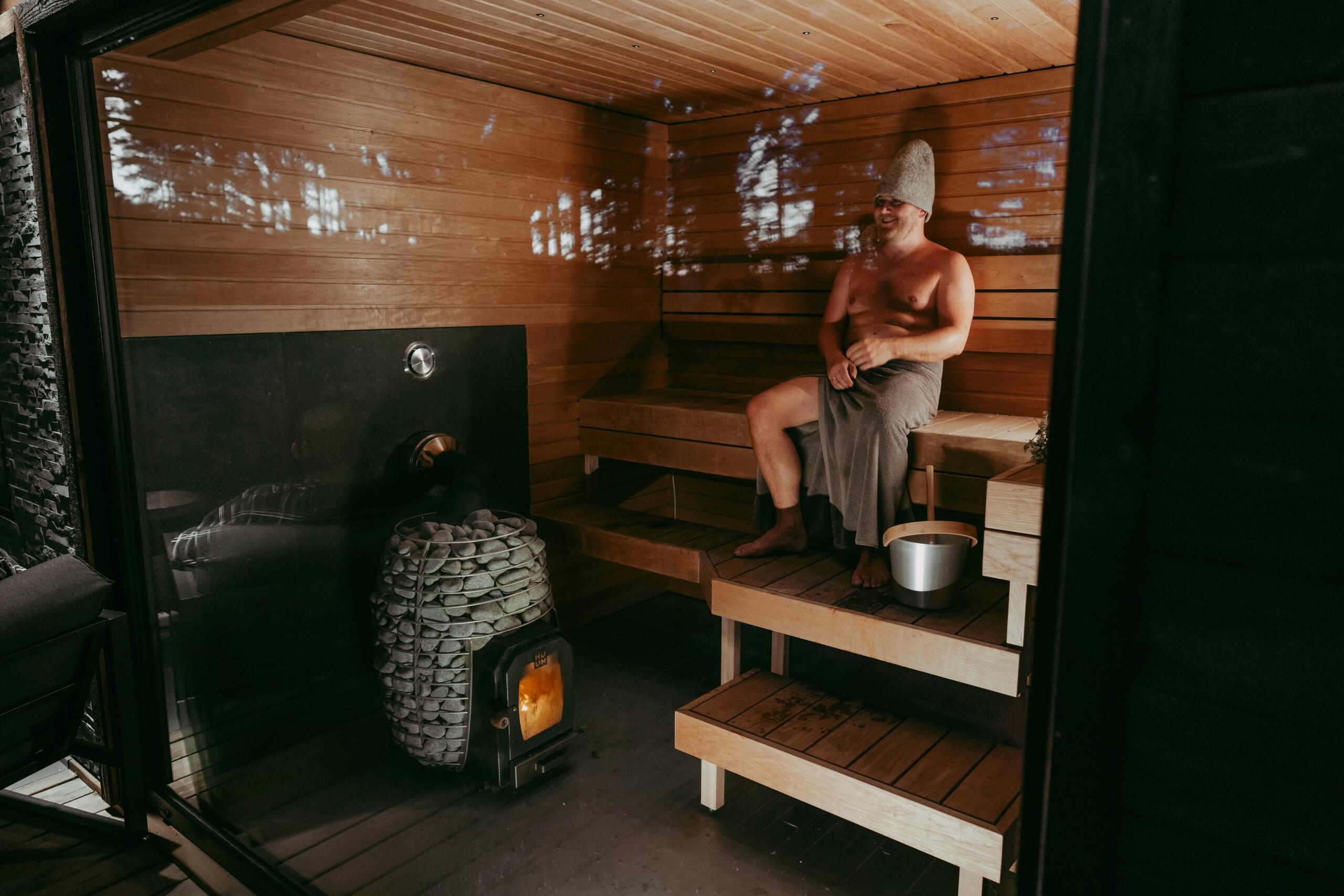 Puidust saunas istub laval rätikuga kaetud mees, peas saunamüts. Tema kõrval on keris ja veega ämber
