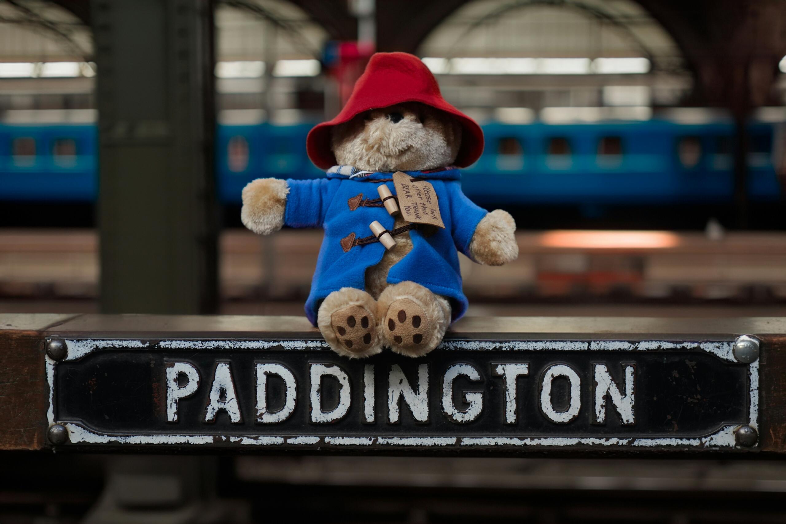 Paddingtoni karu istub Paddingtoni jaama sildil, taustal on rongid ja perroon