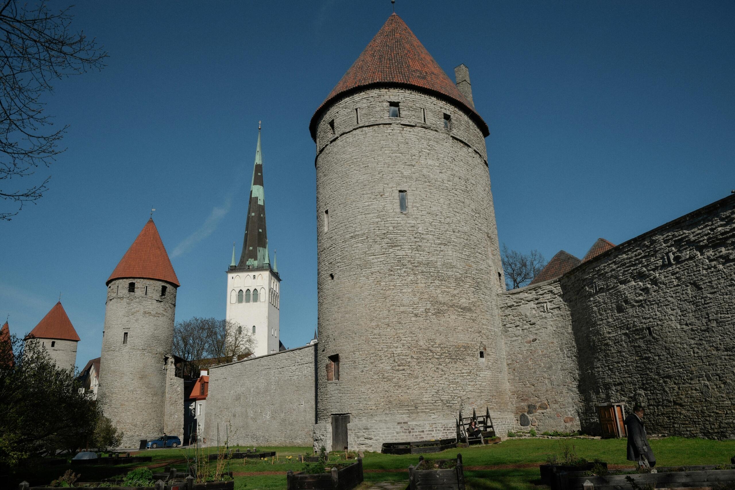Tallinna vanalinna kivimüürid ja tornid punaste katustega, taustal kõrge kirikutorn sinise taeva all