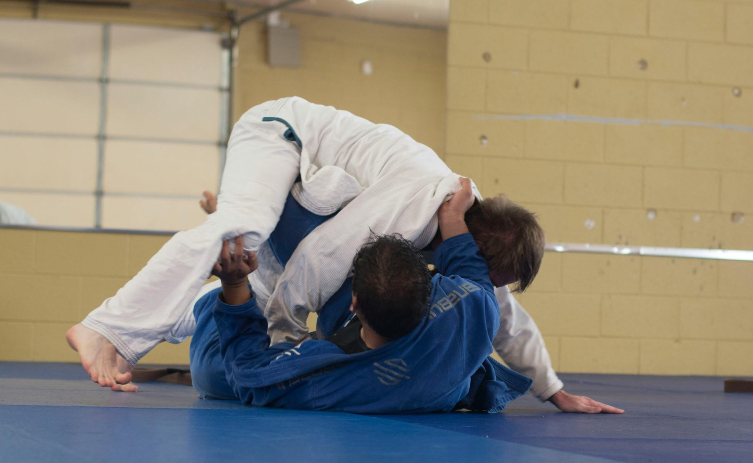 Kaks kimonodes treenijat harjutavad matil Brasiilia jiu-jitsu või judo tehnikat, üks neist on maas ja teine liigub tema kohal kontrollasendisse.