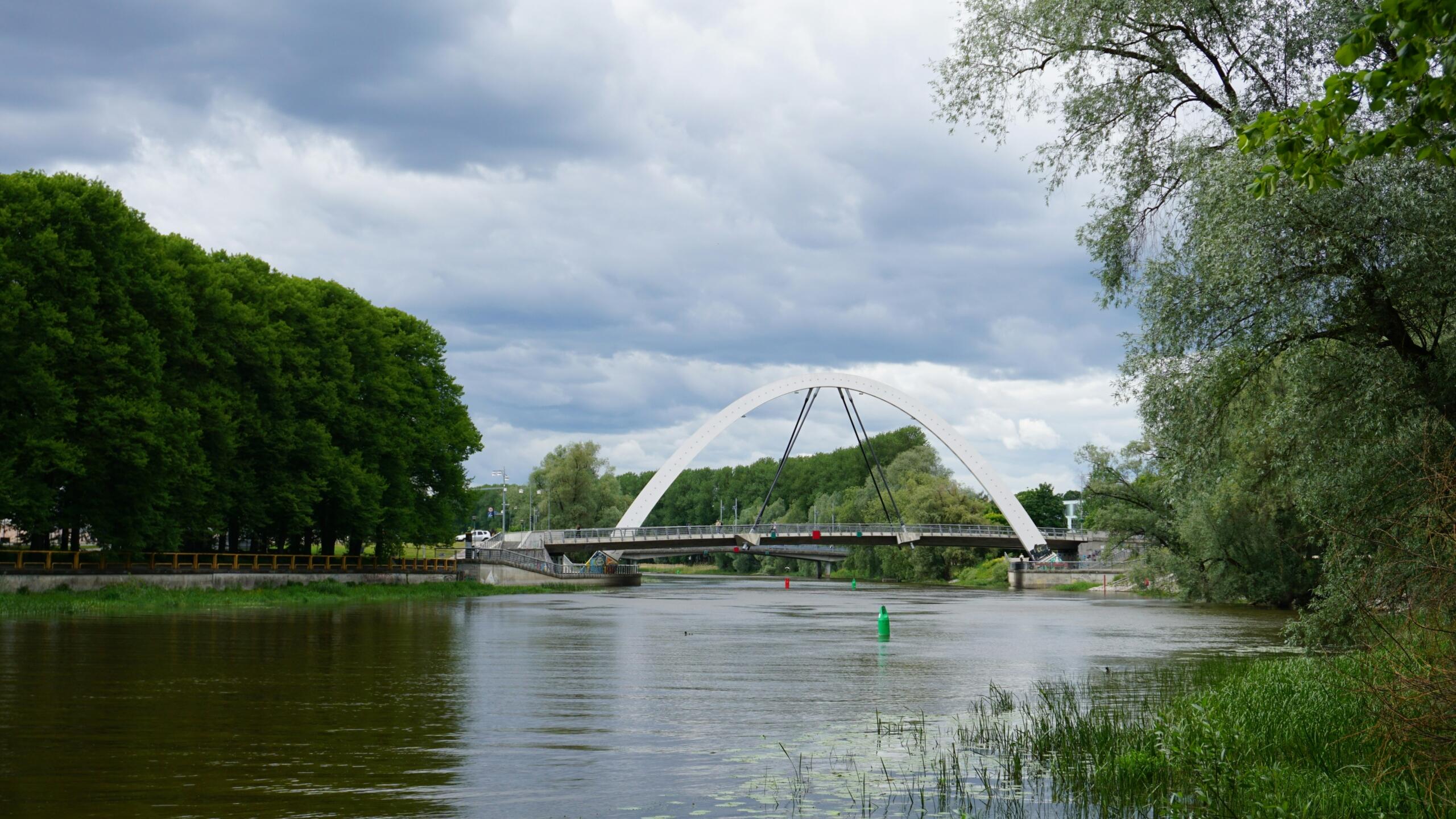 Emajõgi Tartus roheliste kallaste ja valge kaarsillaga pilvise taeva all.