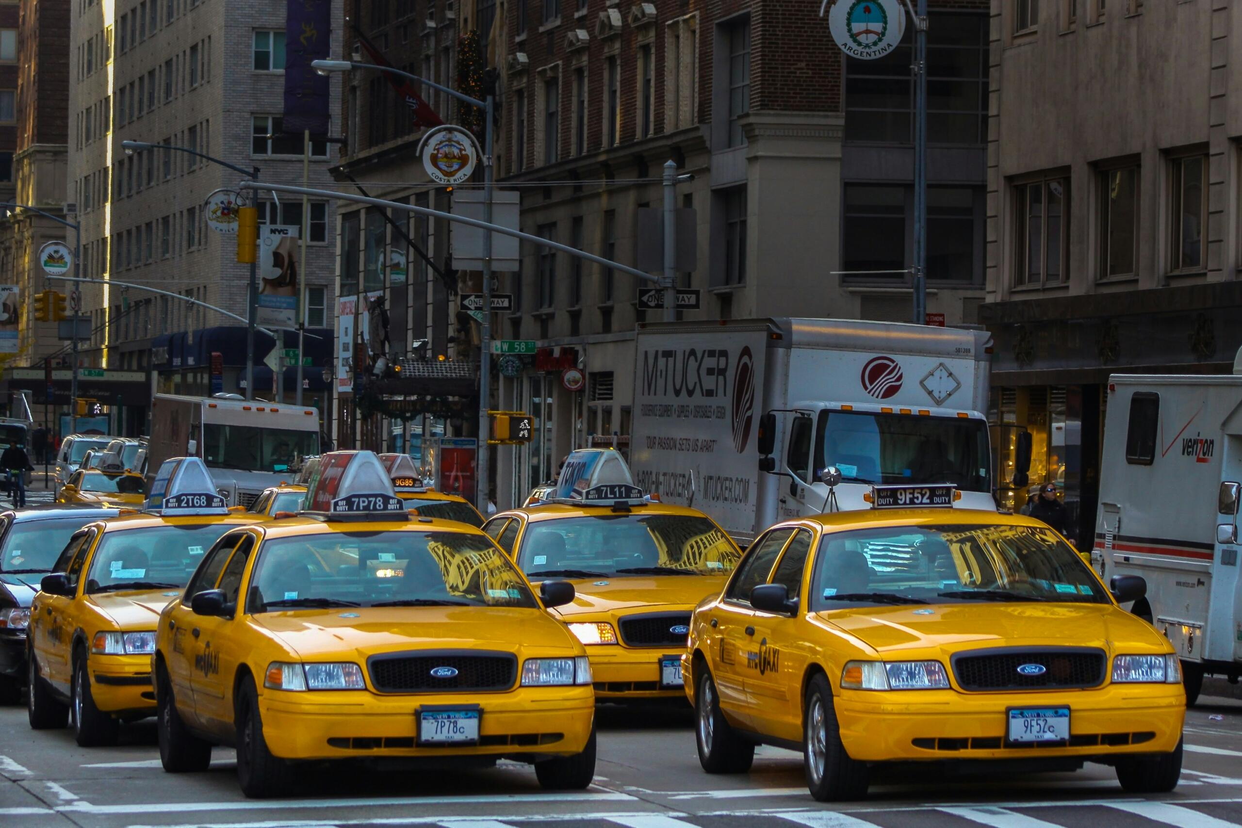 New Yorgi linnatänaval sõidab mitu kollast taksot, taustal kõrged hooned ja tihe liiklus.