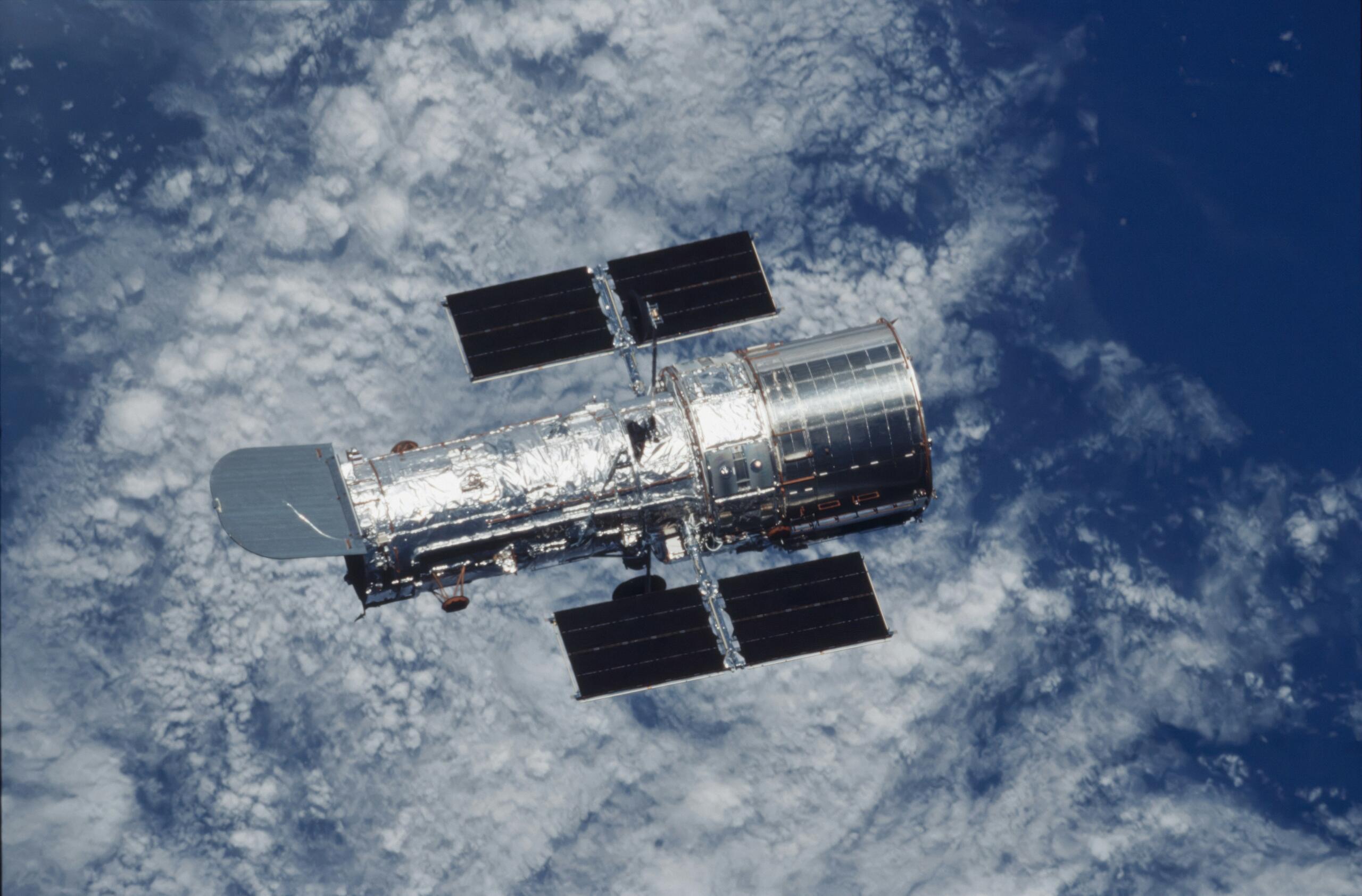 Hubble’i kosmoseteleskoop hõljumas Maa kohal, taustal sinine ookean ja valged pilved.