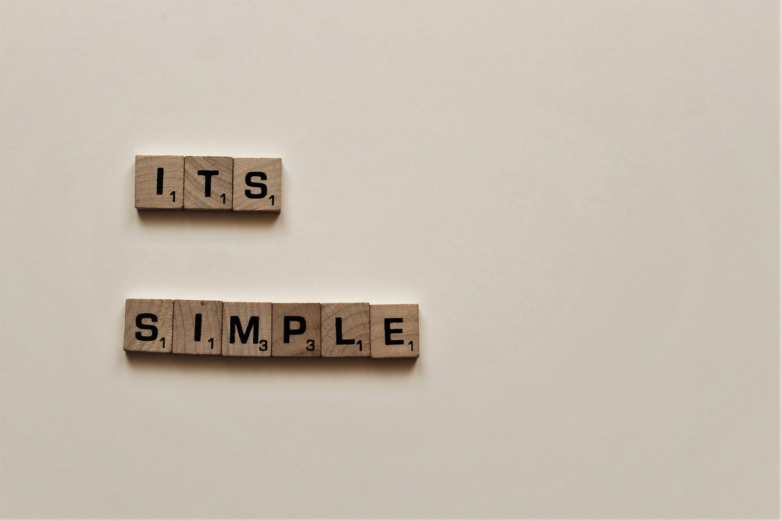 Puidust täheklotsidest moodustatud ingliskeelne fraas „It's simple“ heledal taustal.