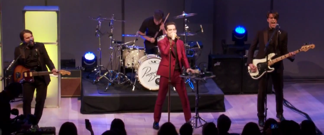Panic! At the Disco esinemas laval, keskel punases ülikonnas laulja ning taustal trummar, kitarrist ja basskitarrist.