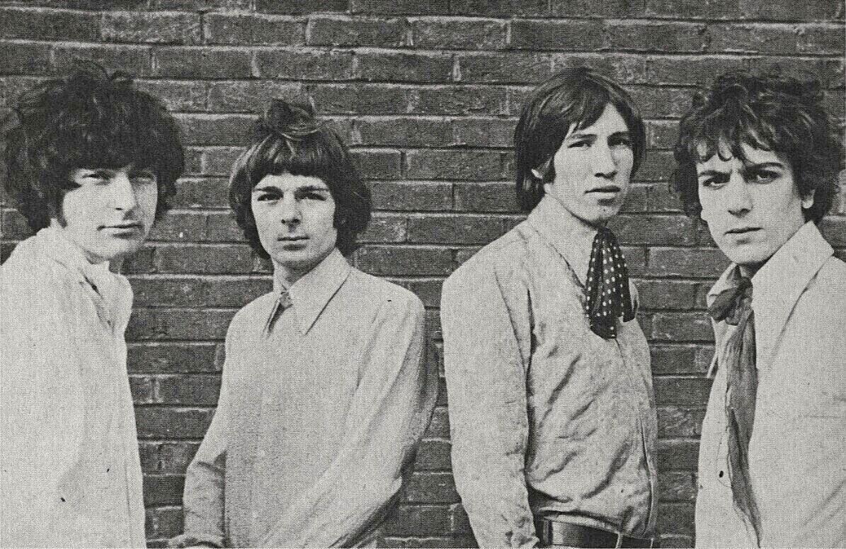 Neli Pink Floydi liiget poseerivad mustvalgel fotol telliskiviseina ees.