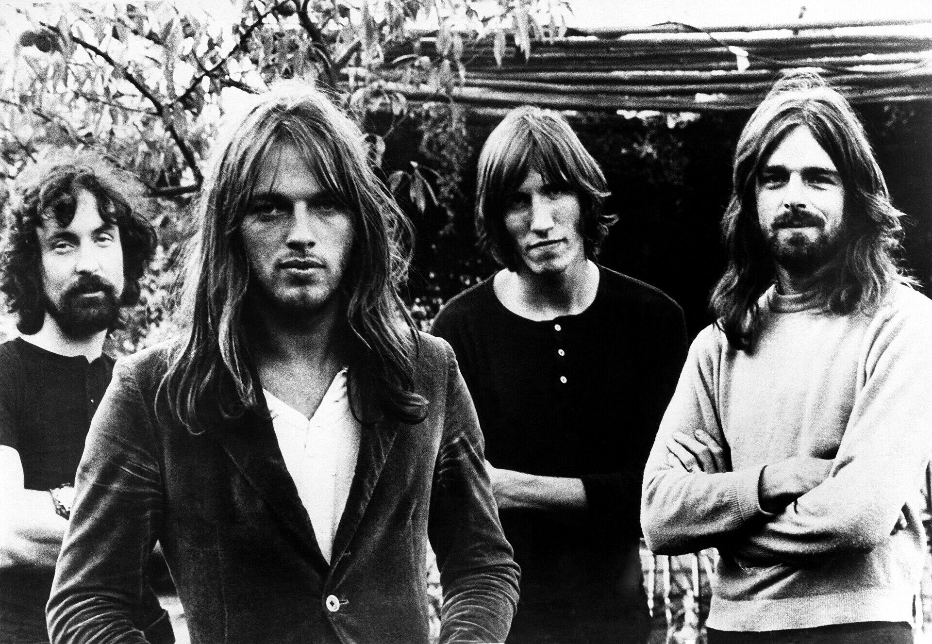 Neli Pink Floydi liiget poseerivad mustvalgel fotol õues puude ja hoone taustal.
