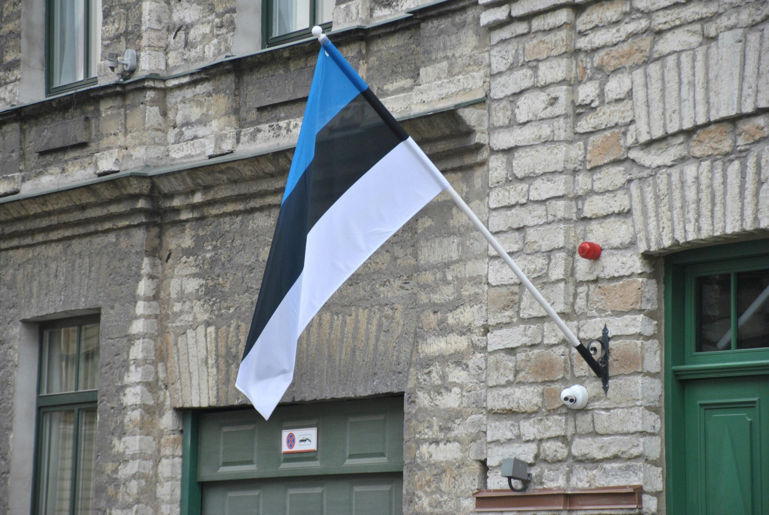 Eesti sinimustvalge lipp lehvib lipuvardal hallist paekivist hoone fassaadi ees.