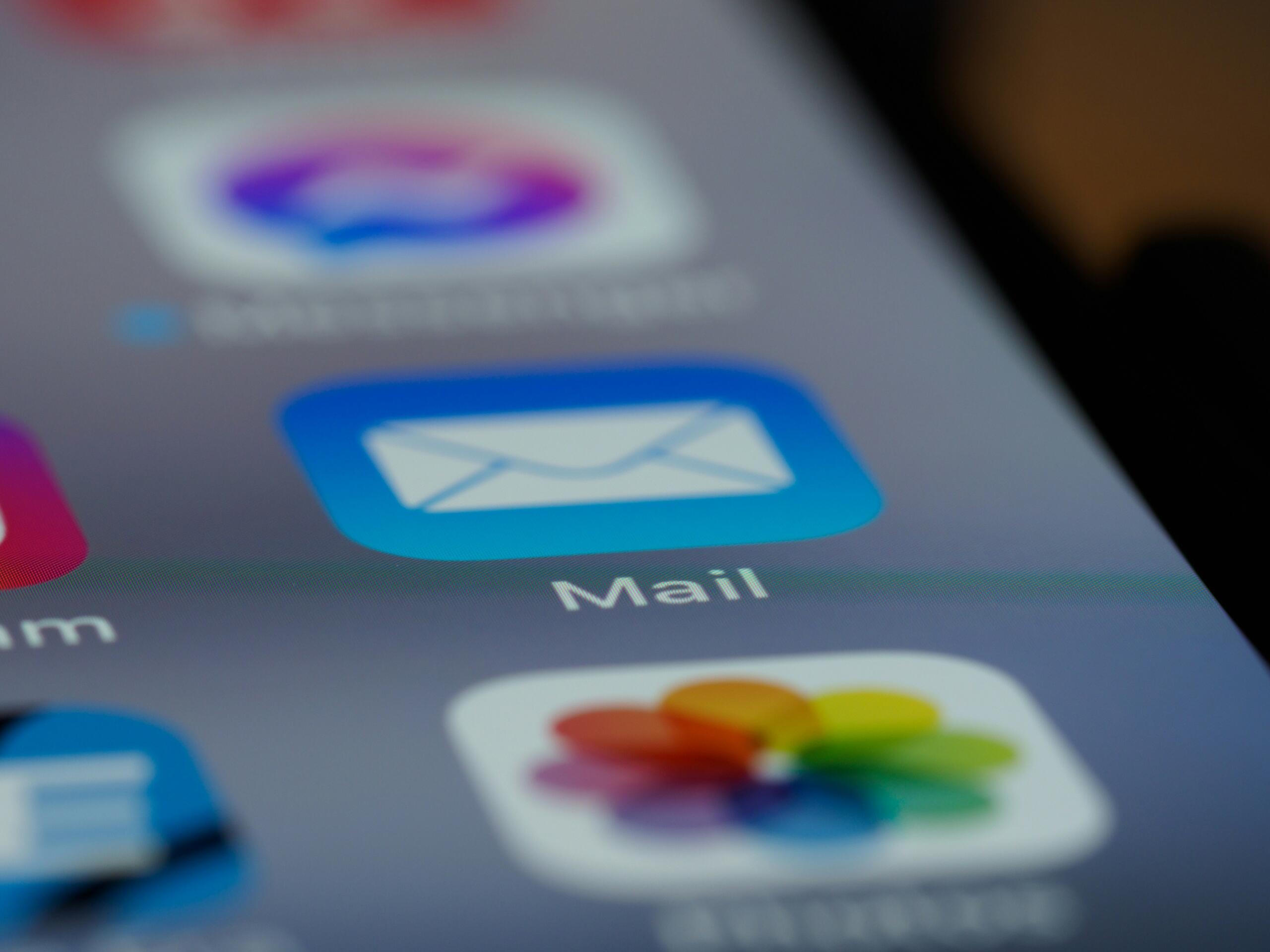 Lähivõte nutitelefoni ekraanist, millel on sinine valge ümbrikuga meilirakenduse ikoon ja selle all kiri „Mail”. Taustal on teised rakenduste ikoonid udused.