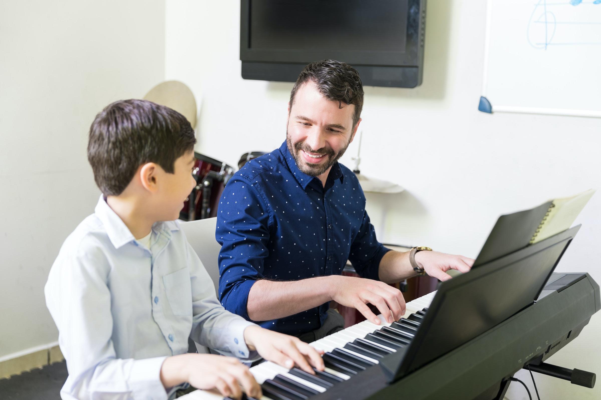 Adulto enseñando piano a niño.