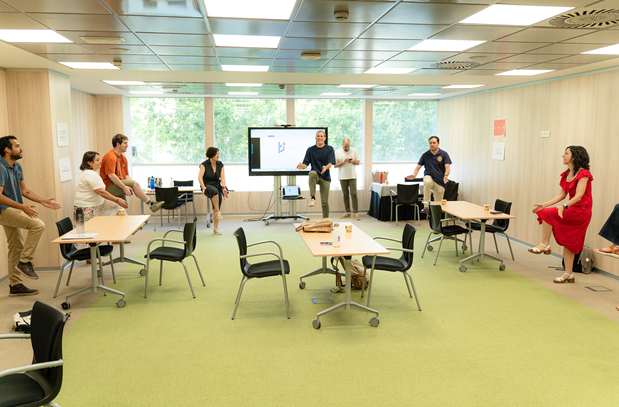 Un grupo de personas vestidas de manera informal participando en un animado ejercicio de trabajo en equipo en una moderna sala de conferencias, creando un ambiente dinámico y colaborativo.