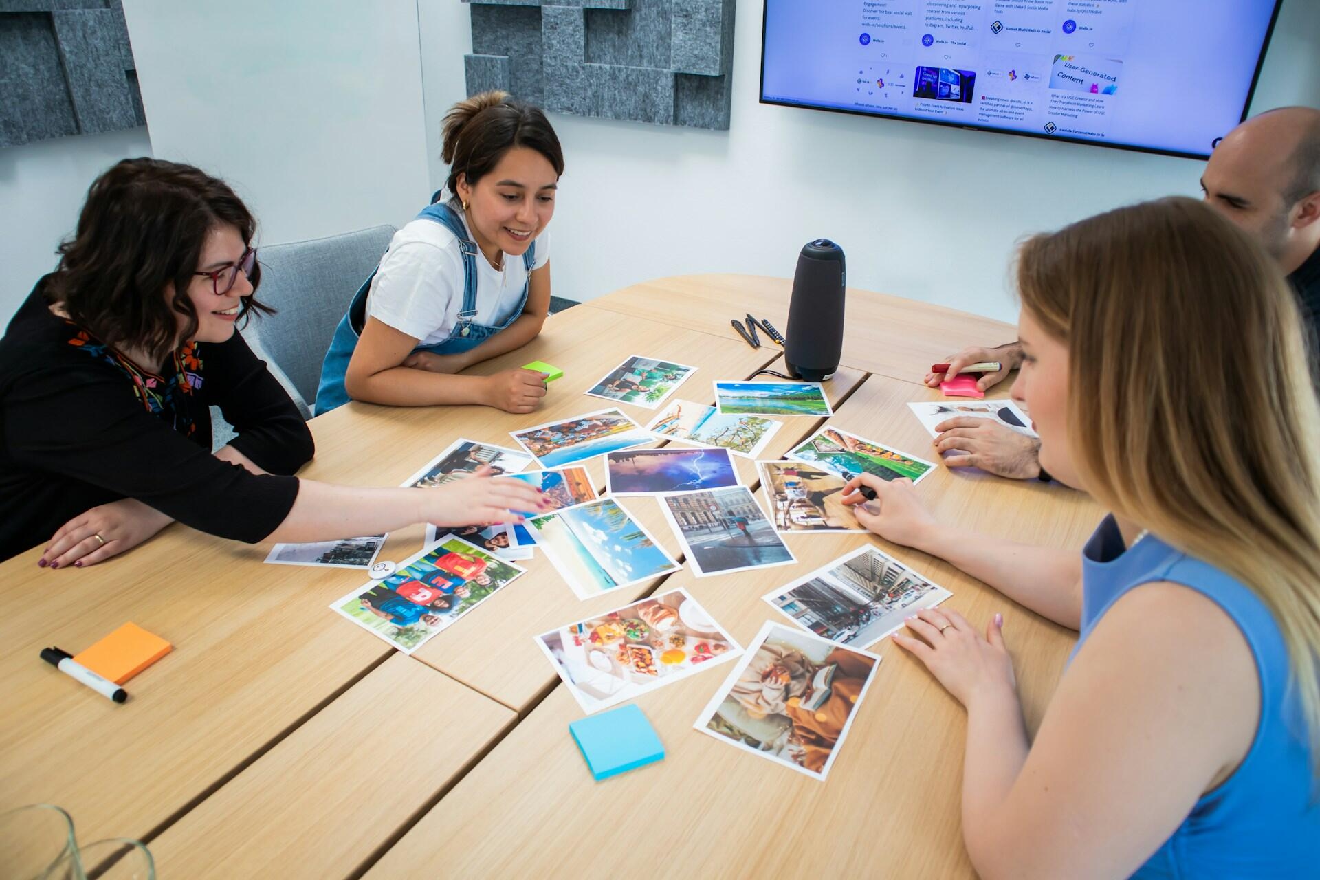 Cuatro personas se reunieron alrededor de una mesa y mantuvieron una conversación creativa con fotografías de colores vivos esparcidas por la mesa, lo que transmitía un espíritu de trabajo en equipo y colaboración.