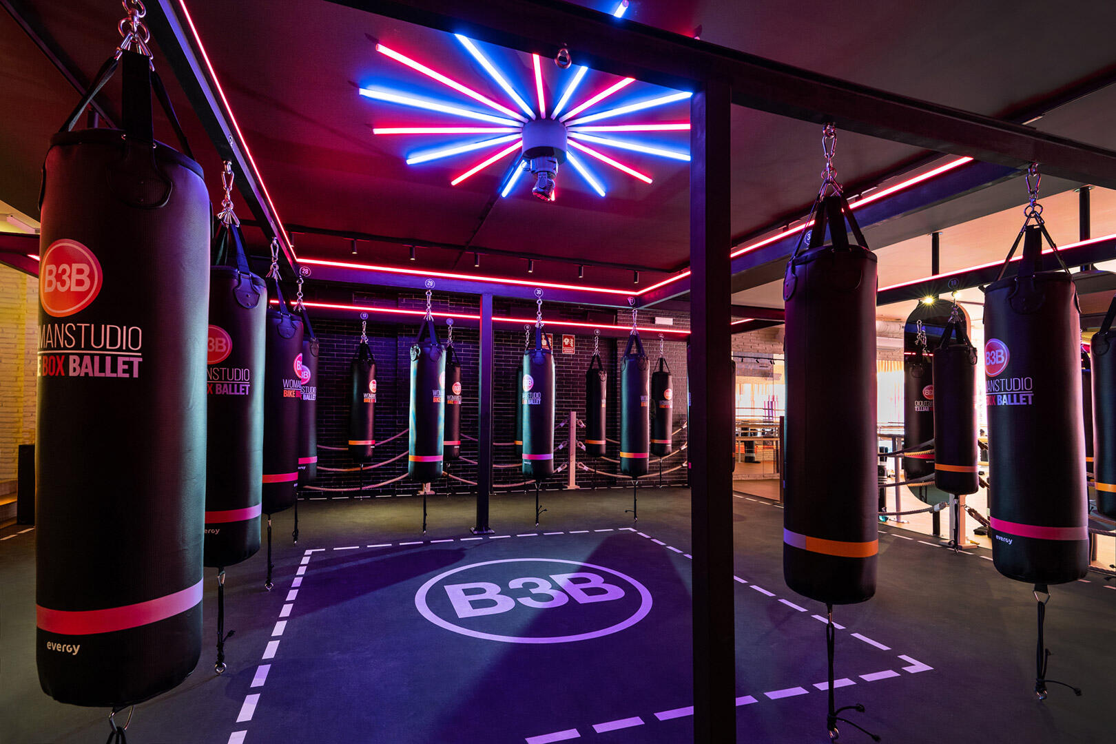 Un gimnasio de boxeo con sacos de boxeo colgantes y luces brillantes iluminando el espacio.