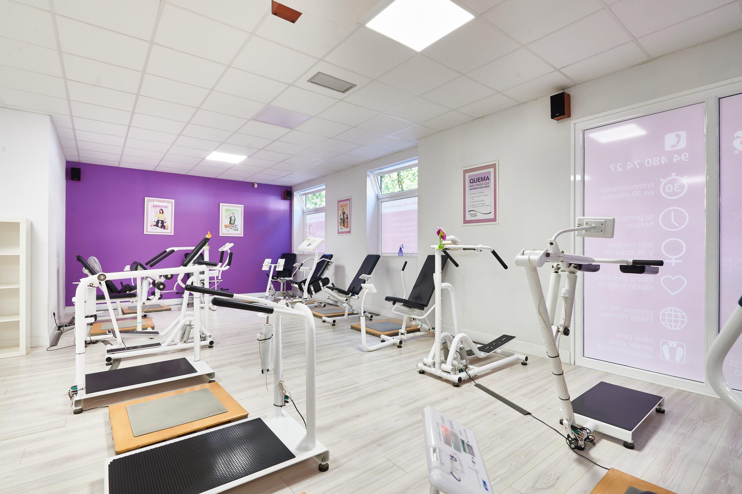 Una sala de gimnasio con diversos equipos de ejercicio frente a paredes de color púrpura intenso.