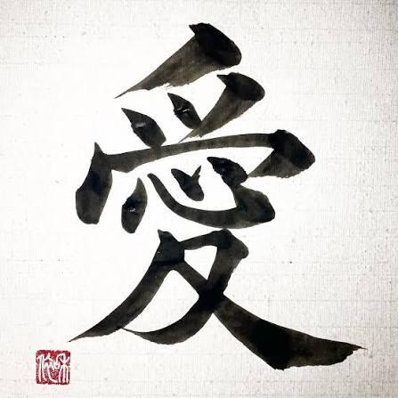 La caligrafía china en negro del carácter «愛» (amor) está centrada sobre un papel blanco con textura, con trazos de pincel expresivos y marcados, y un sello rojo en la parte inferior izquierda, lo que transmite tradición y emoción.
