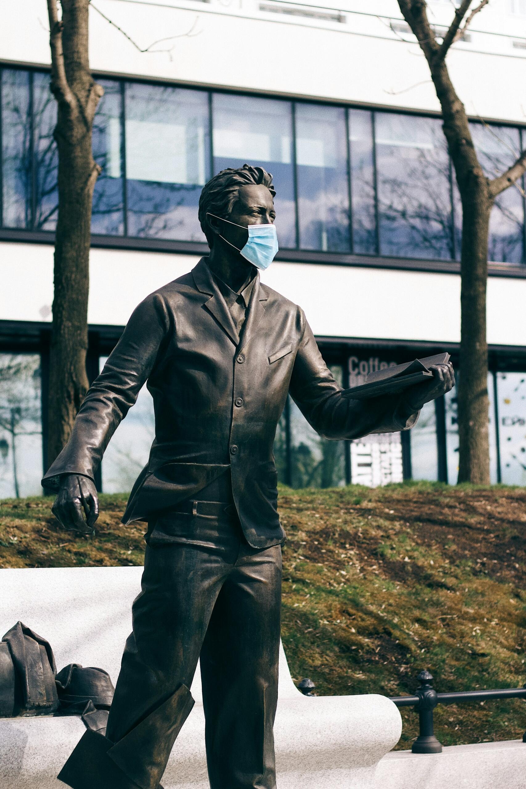 Una estatua de una persona con traje que sostiene un libro, con una cafetería al fondo.