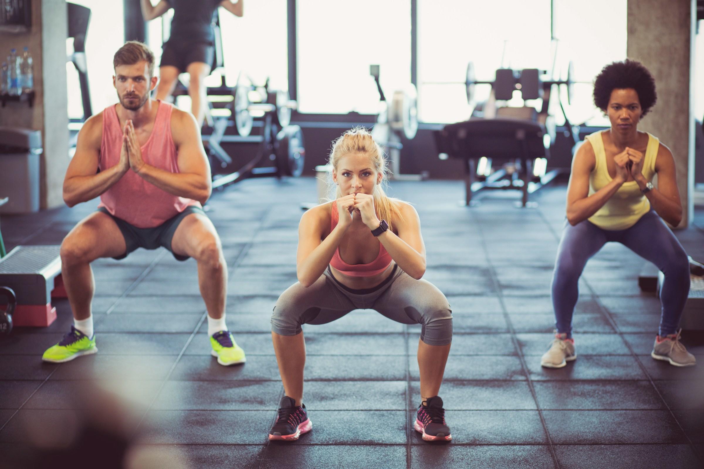 Tres personas haciendo una sentadilla en el gimnasio.