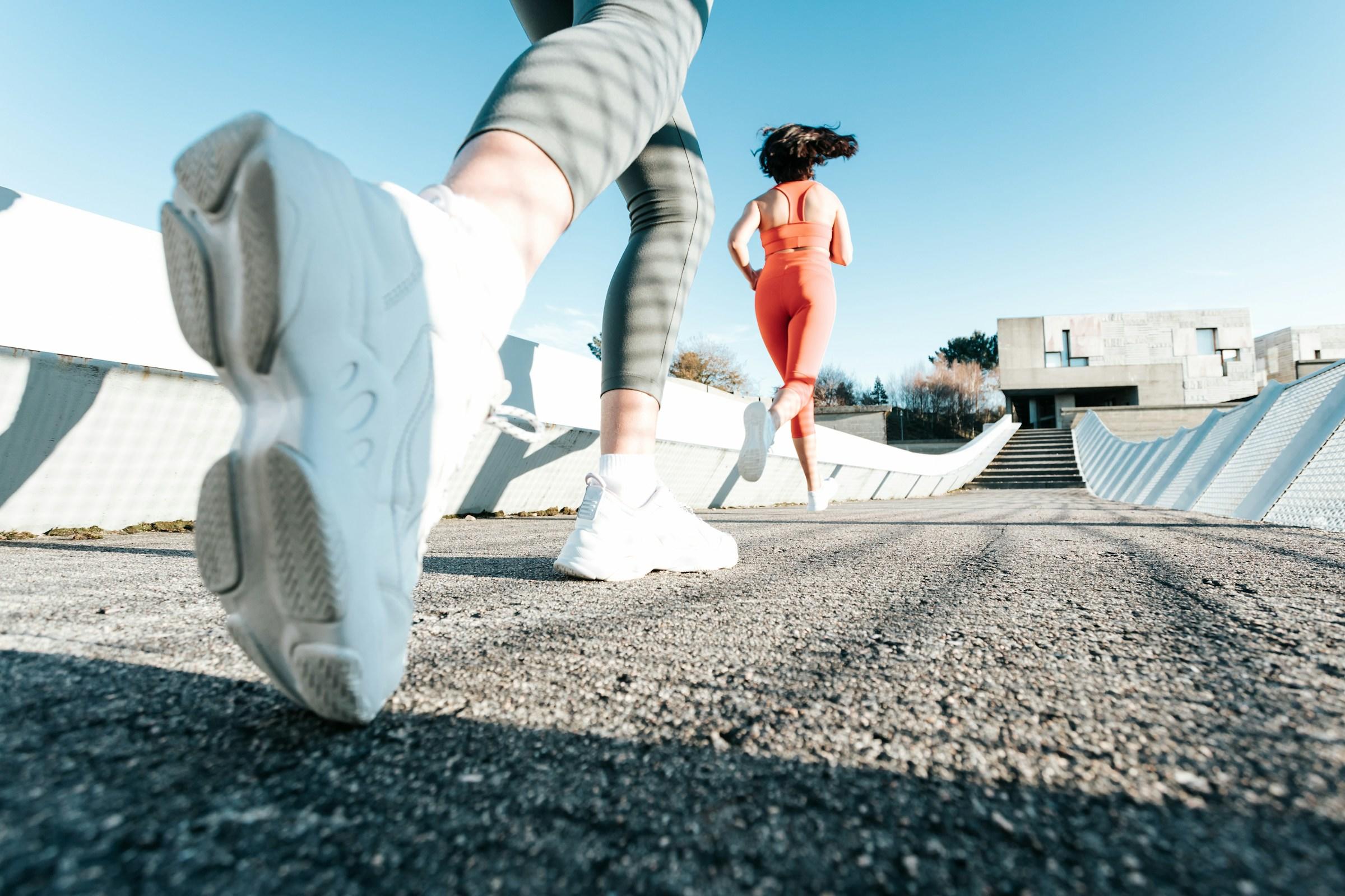 Dos personas haciendo footing al aire libre, foco en los zapatos con escaleras urbanas de fondo.