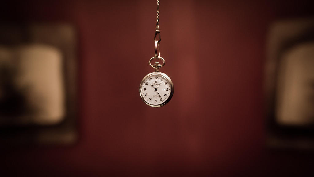 Reloj de bolsillo colgando sobre un fondo desenfocado.