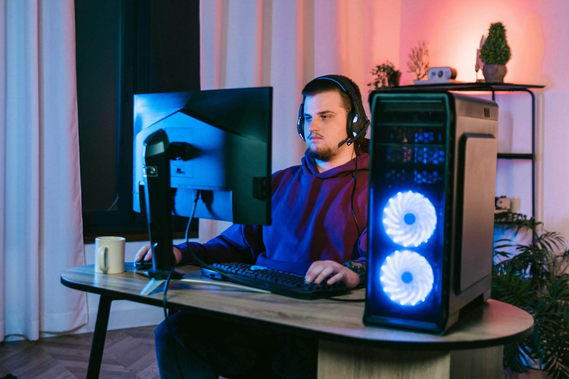 Persona en un escritorio con un PC para juegos, con auriculares y un teclado retroiluminado.