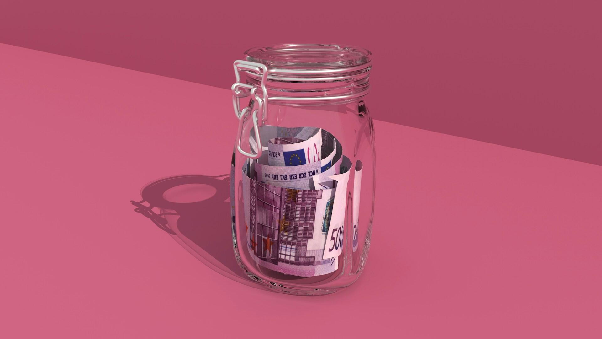 Un tarro de cristal con un billete de 500 euros enrollado en su interior sobre fondo rosa.