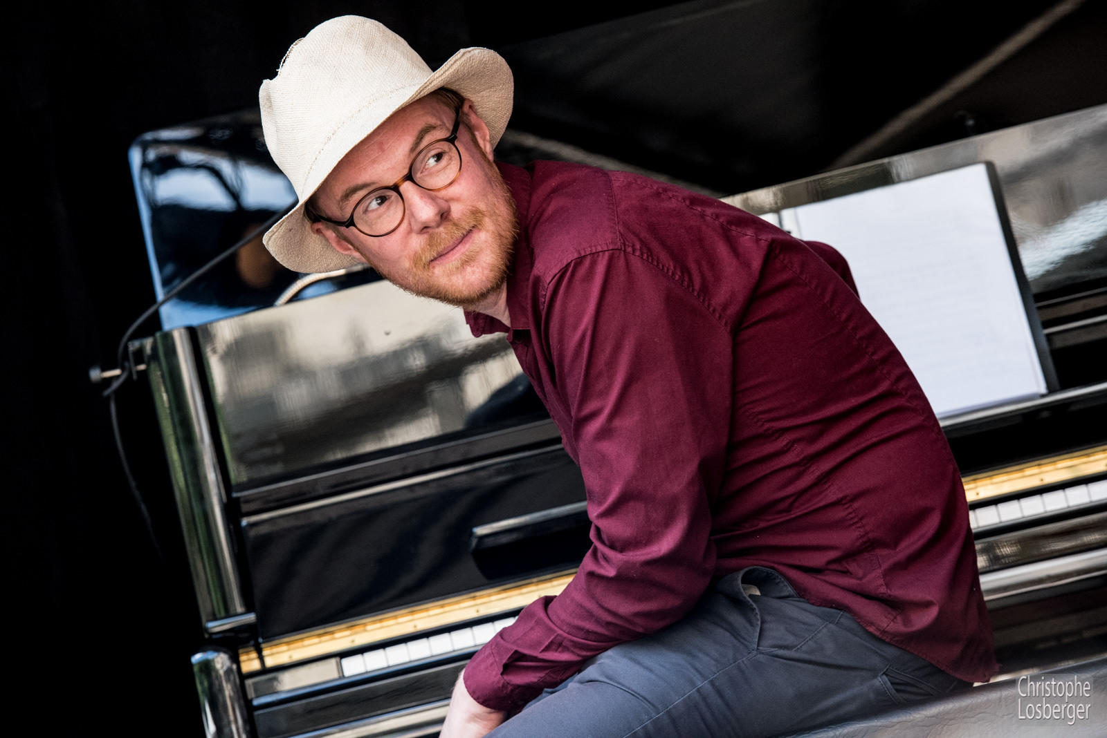Hombre con sombrero y gafas sentado frente al piano mirando fijamente hacia el otro lado