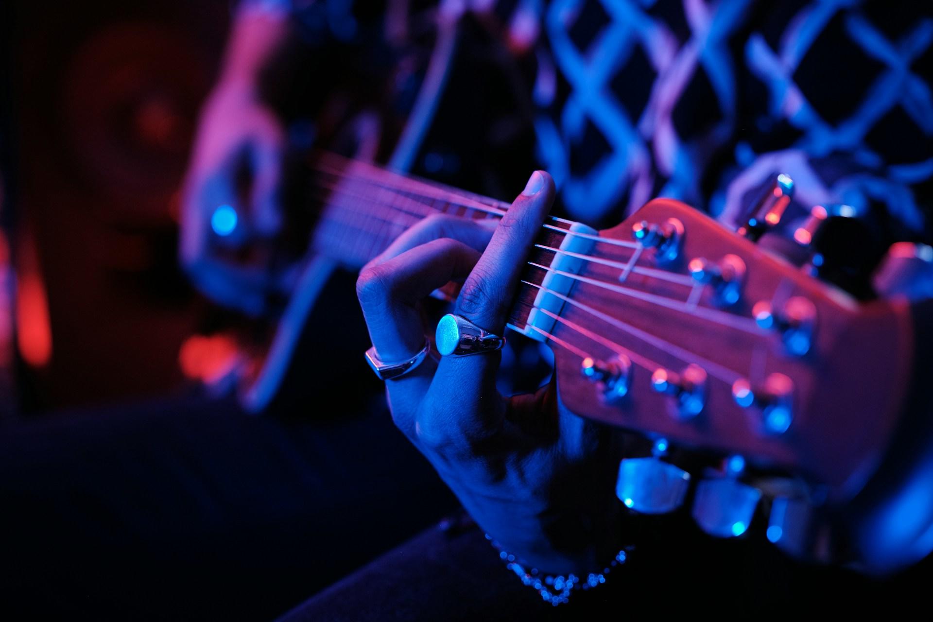 Primer plano de una mano tocando una guitarra bajo una iluminación azul.
