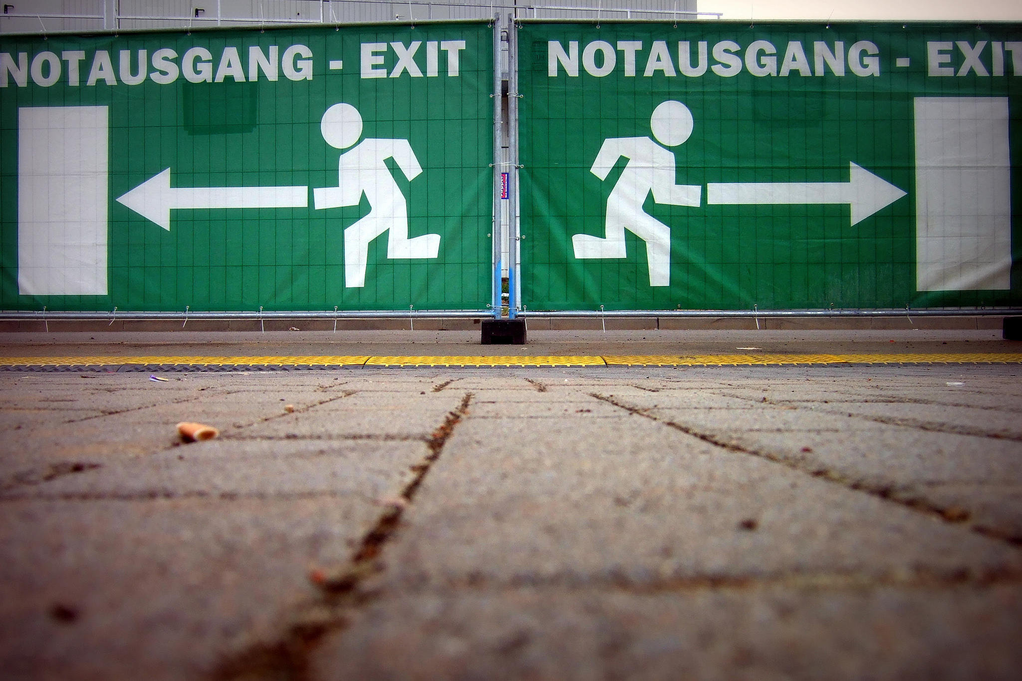 Carteles verdes con señales de salida de emergencia con figuras corriendo y flechas apuntando hacia la izquierda, con la inscripción «NOTAUSGANG - EXIT».