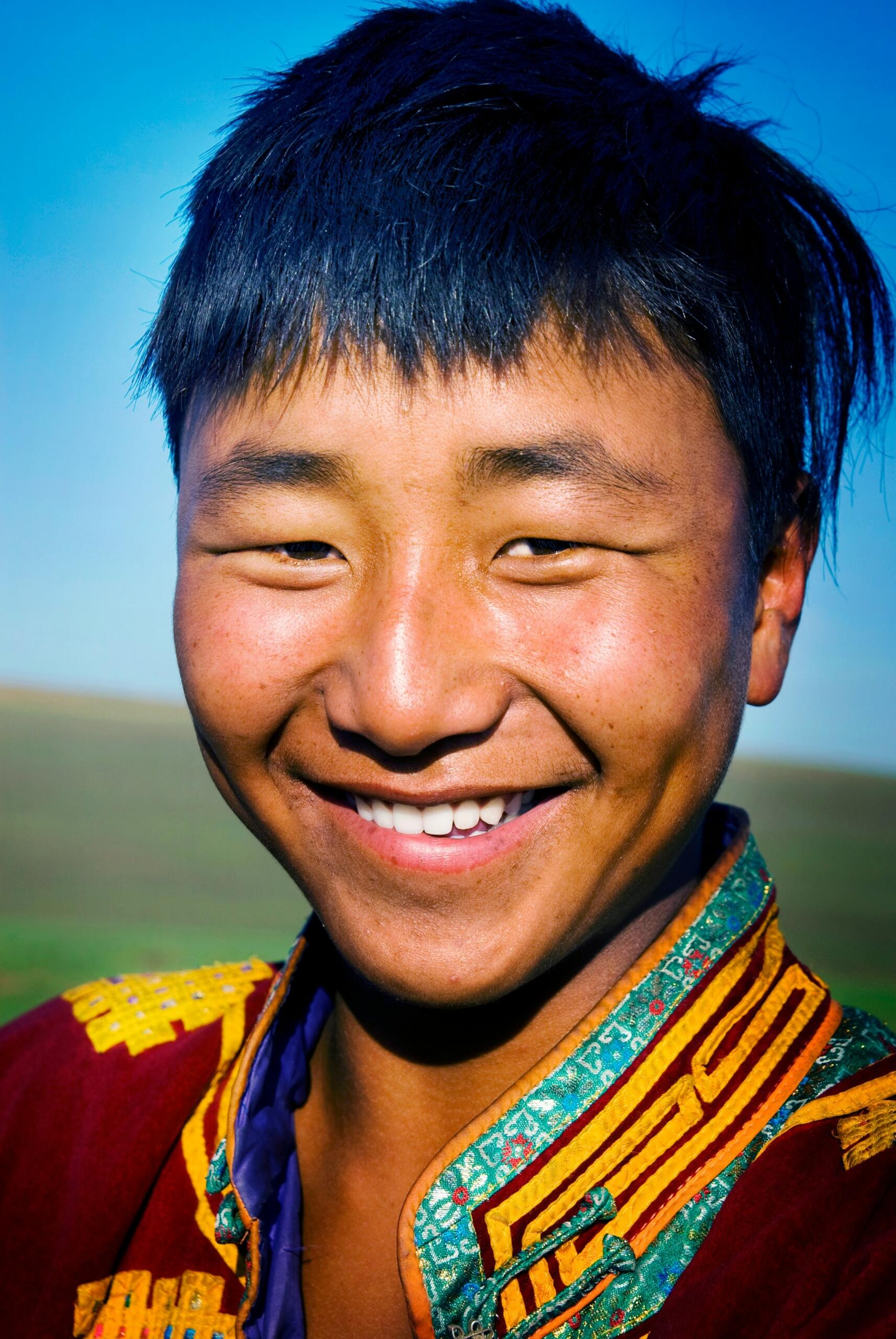 Una persona que lleva un traje tradicional de colores vivos con motivos intrincados, con un cielo azul claro y un paisaje abierto como telón de fondo.