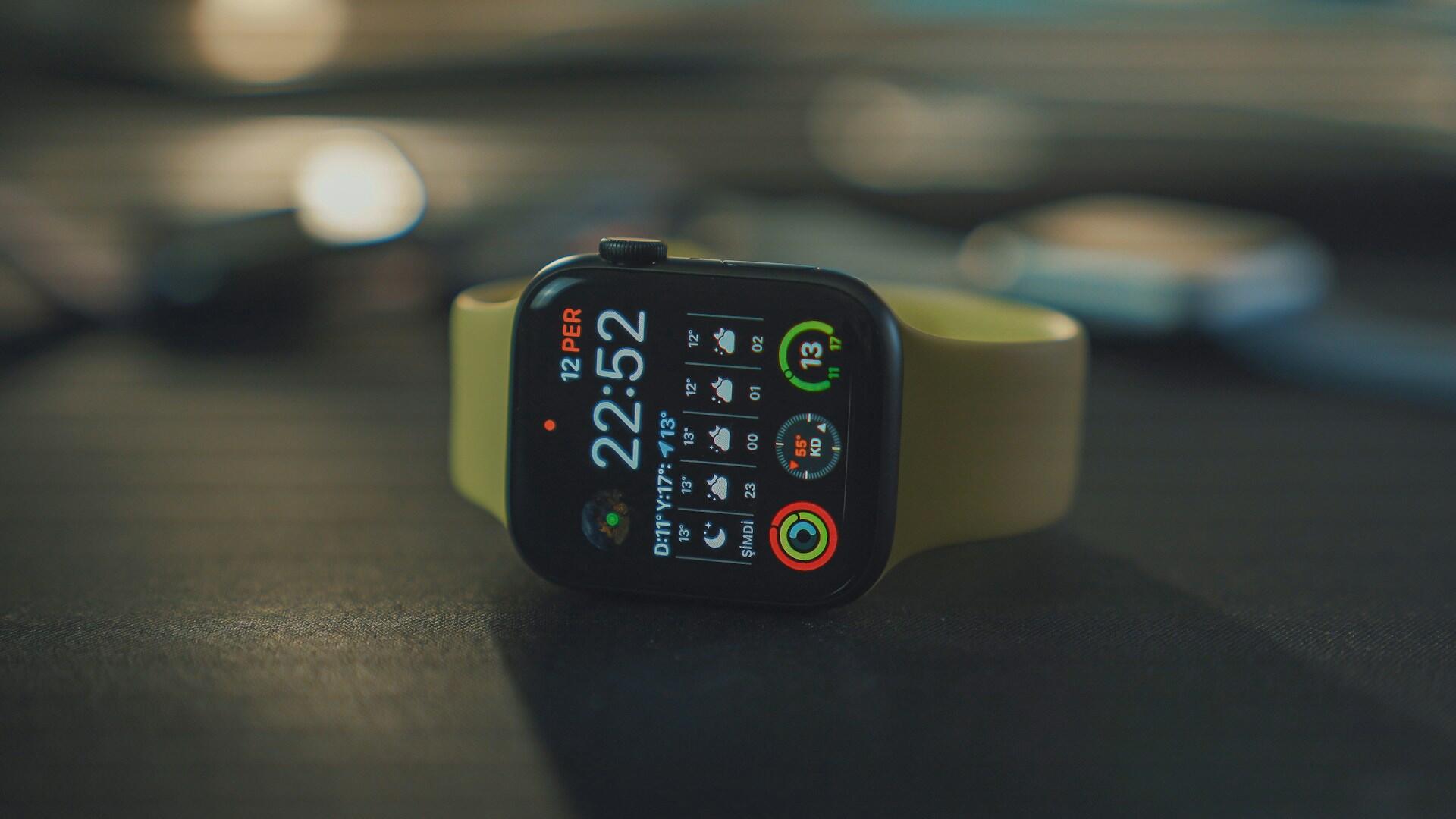 Primer plano de un reloj inteligente con correa verde que muestra las 22:52 y varios iconos de aplicaciones de colores. El fondo está ligeramente desenfocado, lo que transmite un ambiente tecnológico.