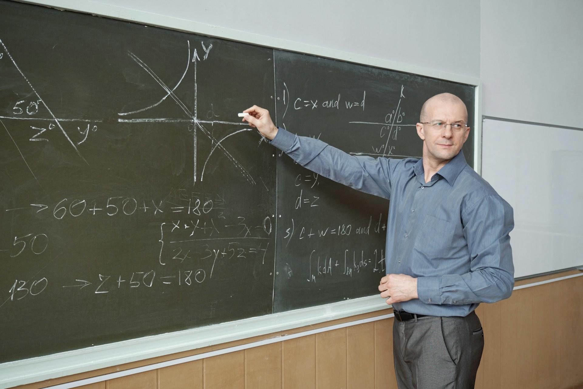 Persona señalando ecuaciones matemáticas en una pizarra de una clase.