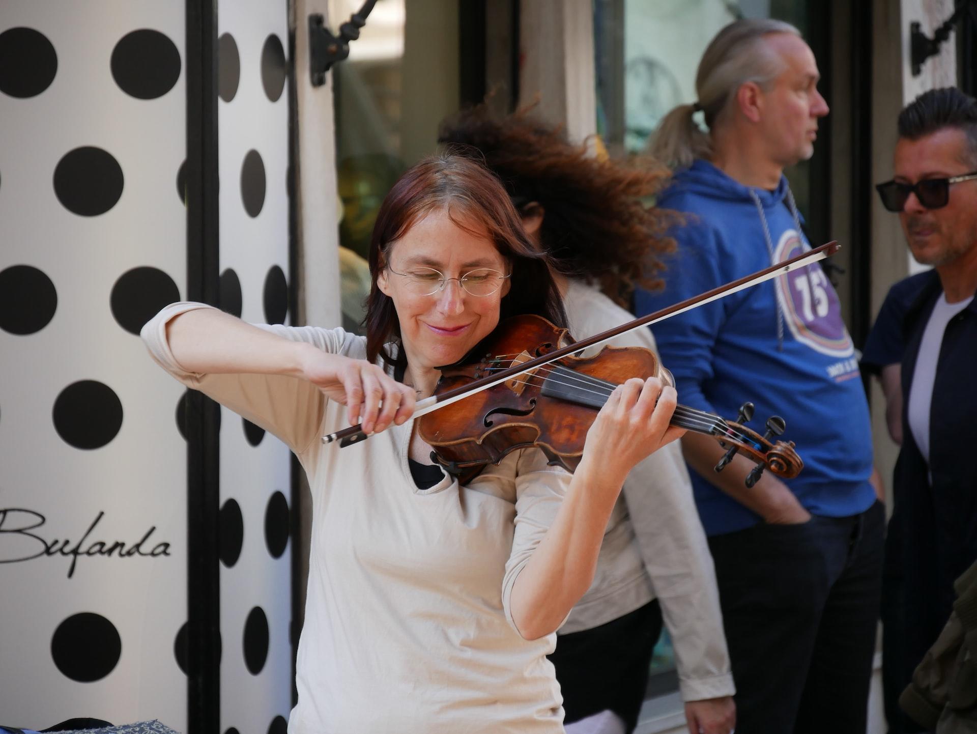 Mujer tocando el violín con cara de alegría.