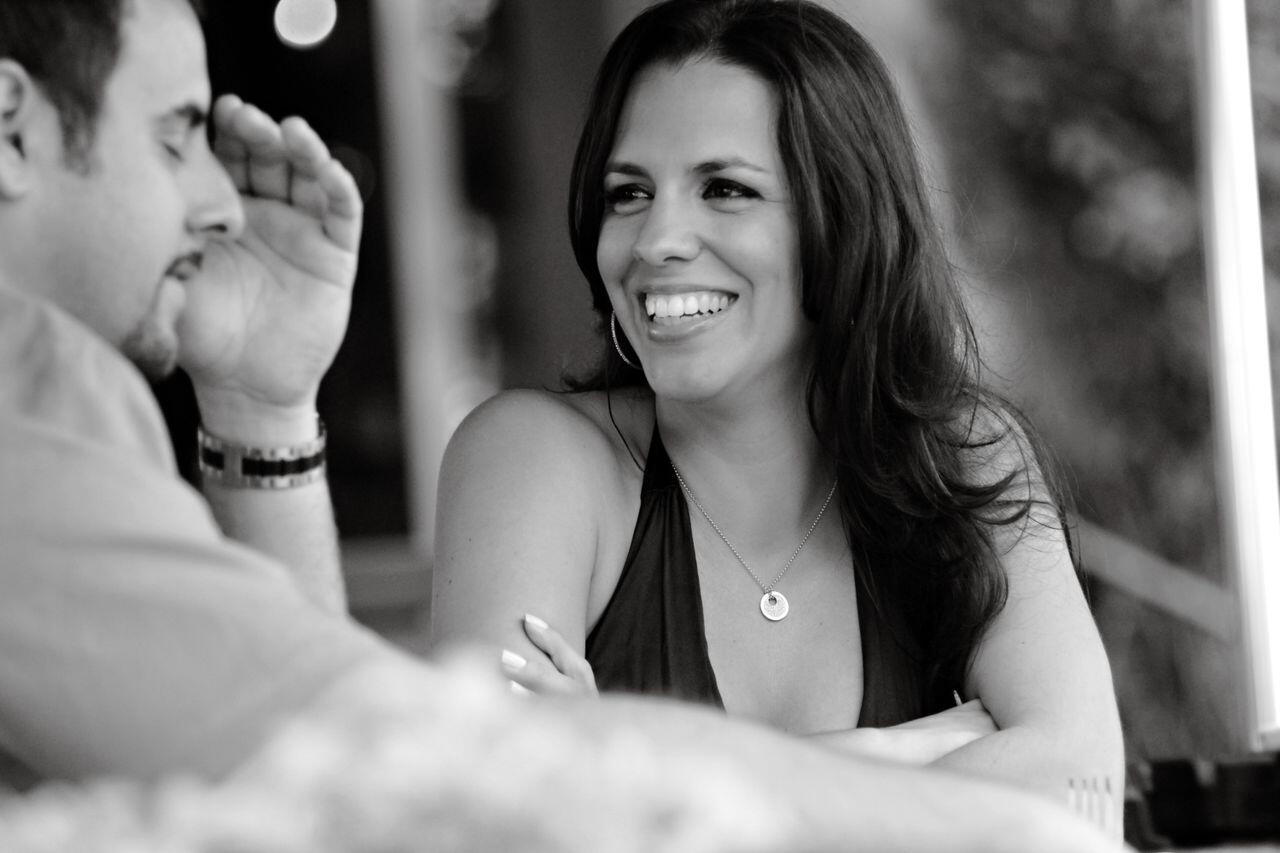 Fotografía en blanco y negro de una mujer sonriente charlando con un hombre en una cafetería, que transmite un ambiente cálido y relajado durante una conversación amistosa.