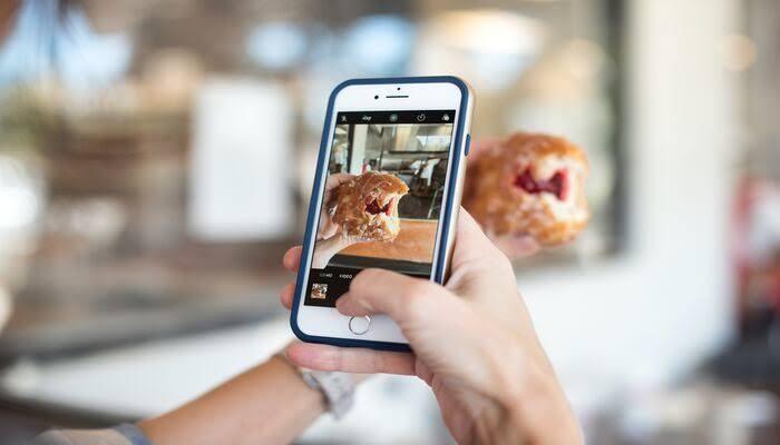Primer plano de una persona que fotografía una rosquilla mordida con un smartphone. Se ve claramente el relleno de mermelada de la rosquilla y el fondo aparece ligeramente desenfocado.