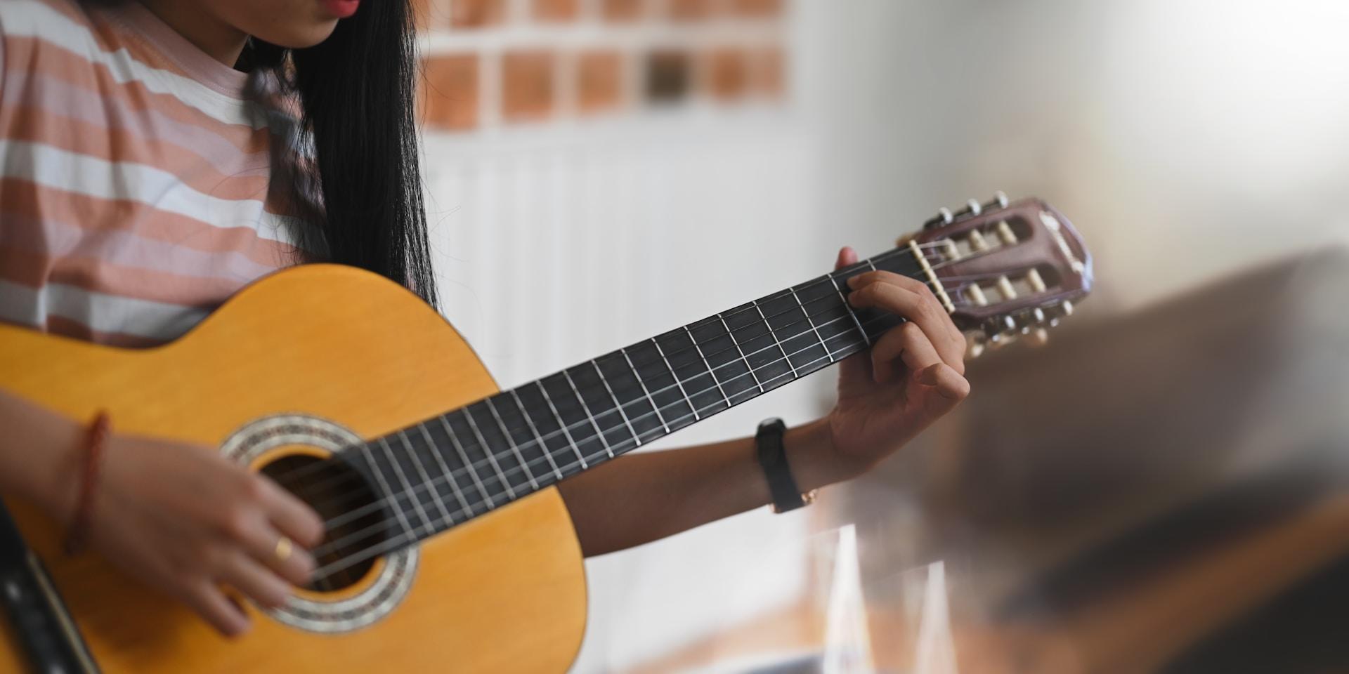 Persona tocando acordes en una guitarra acústica, primer plano de las manos.