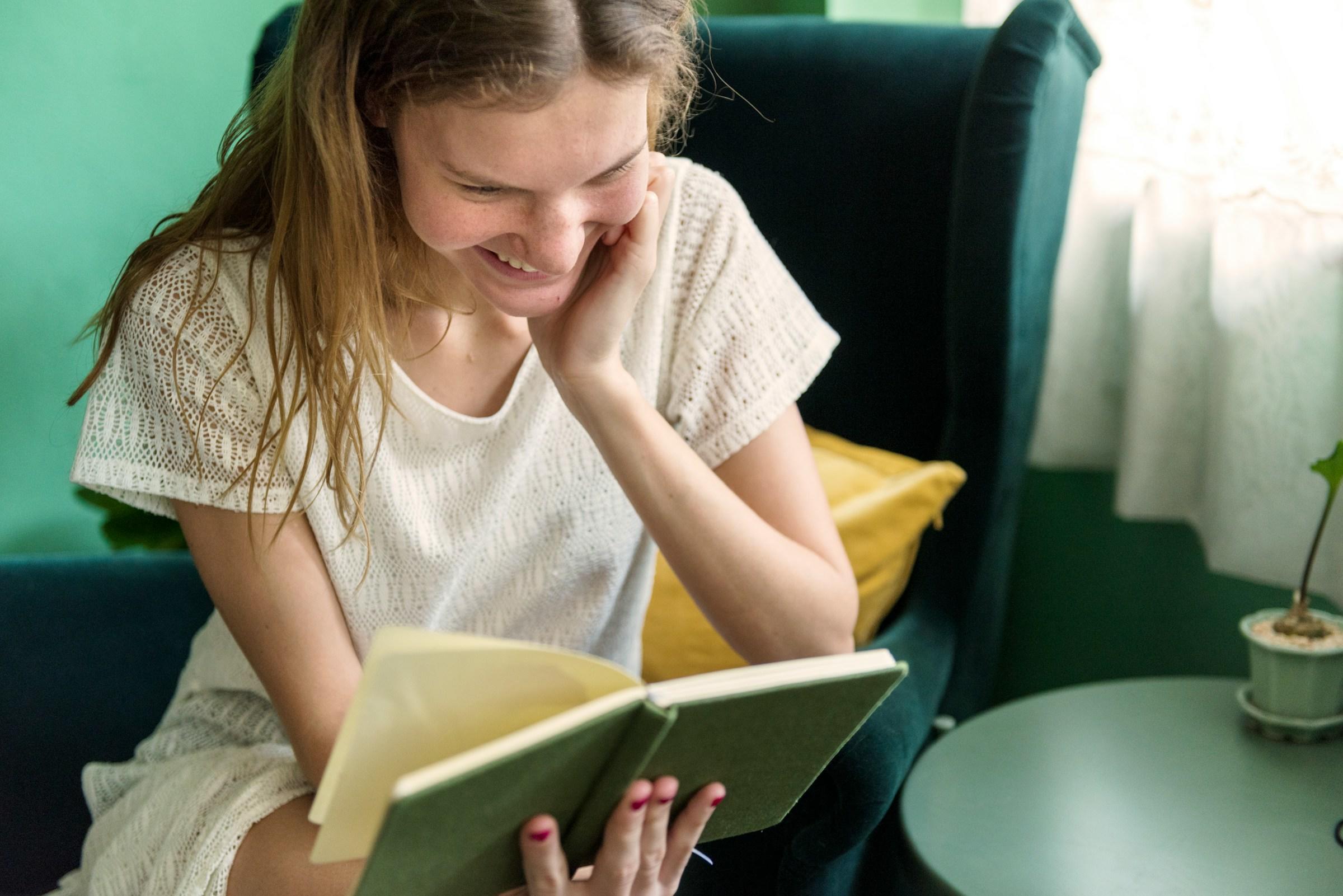 Mujer vestida de blanco leyendo un libro en un sillón verde.