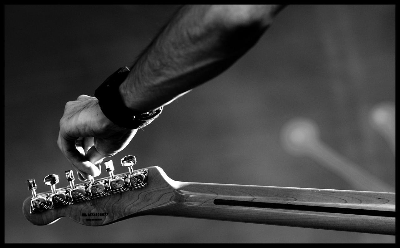 Mano de un chico sobre el clavijero de una guitarra, con la intención de afinarla.