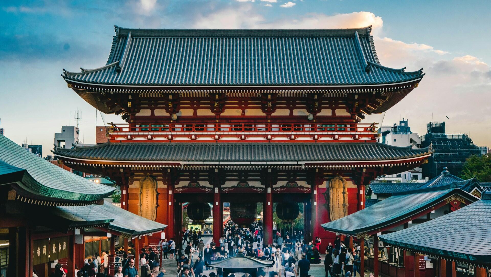 La ornamentada puerta Hozomon del templo Senso-ji, en Tokio, con sus pilares rojos, sus amplios tejados de tejas, la multitud de visitantes y un ambiente alegre y animado.
