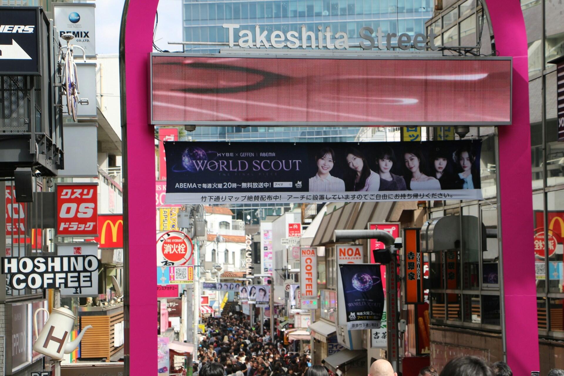 La concurrida calle Takeshita de Tokio, enmarcada por un arco rosa, con coloridos letreros japoneses, tiendas, anuncios y una densa multitud que crea un ambiente lleno de energía.