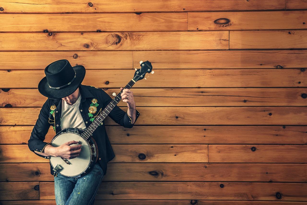 chico apoyado contra un muro de madera con su banjo en manos