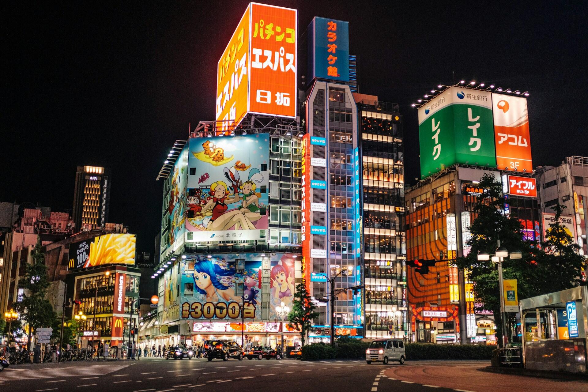 Un cruce nocturno de Tokio que resplandece con coloridas vallas publicitarias japonesas, anuncios de anime, rascacielos de oficinas, tráfico y peatones, en una escena llena de vida.