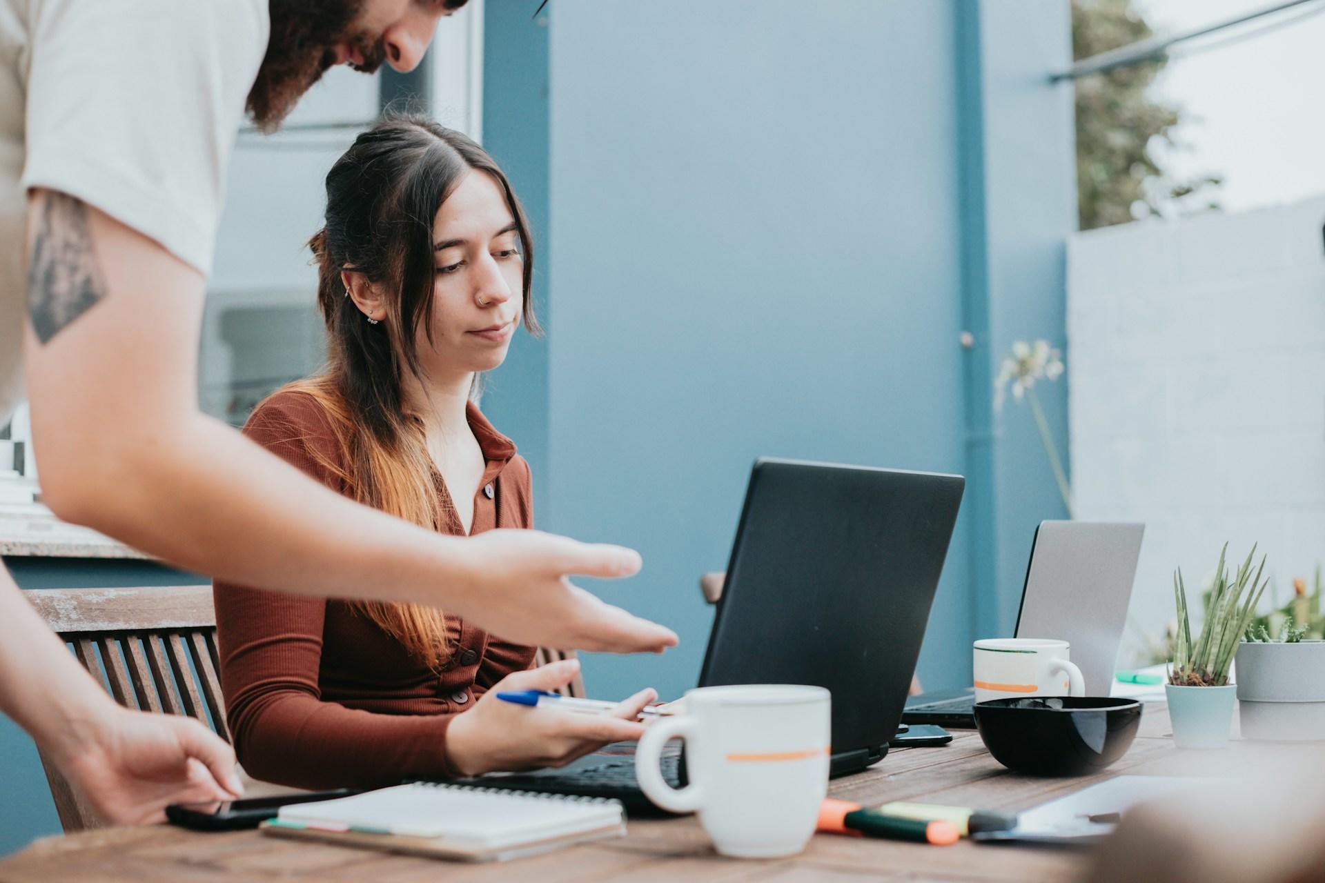 Dos personas colaborando en una mesa con ordenadores portátiles y blocs de notas.