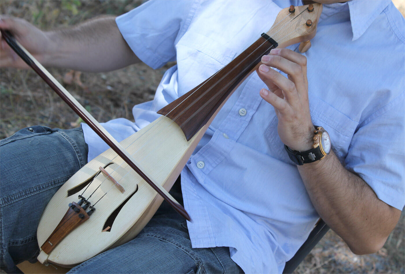 Una persona con una camisa azul claro toca un instrumento de cuerda de madera, sosteniendo el arco con una mano y el instrumento con la otra.