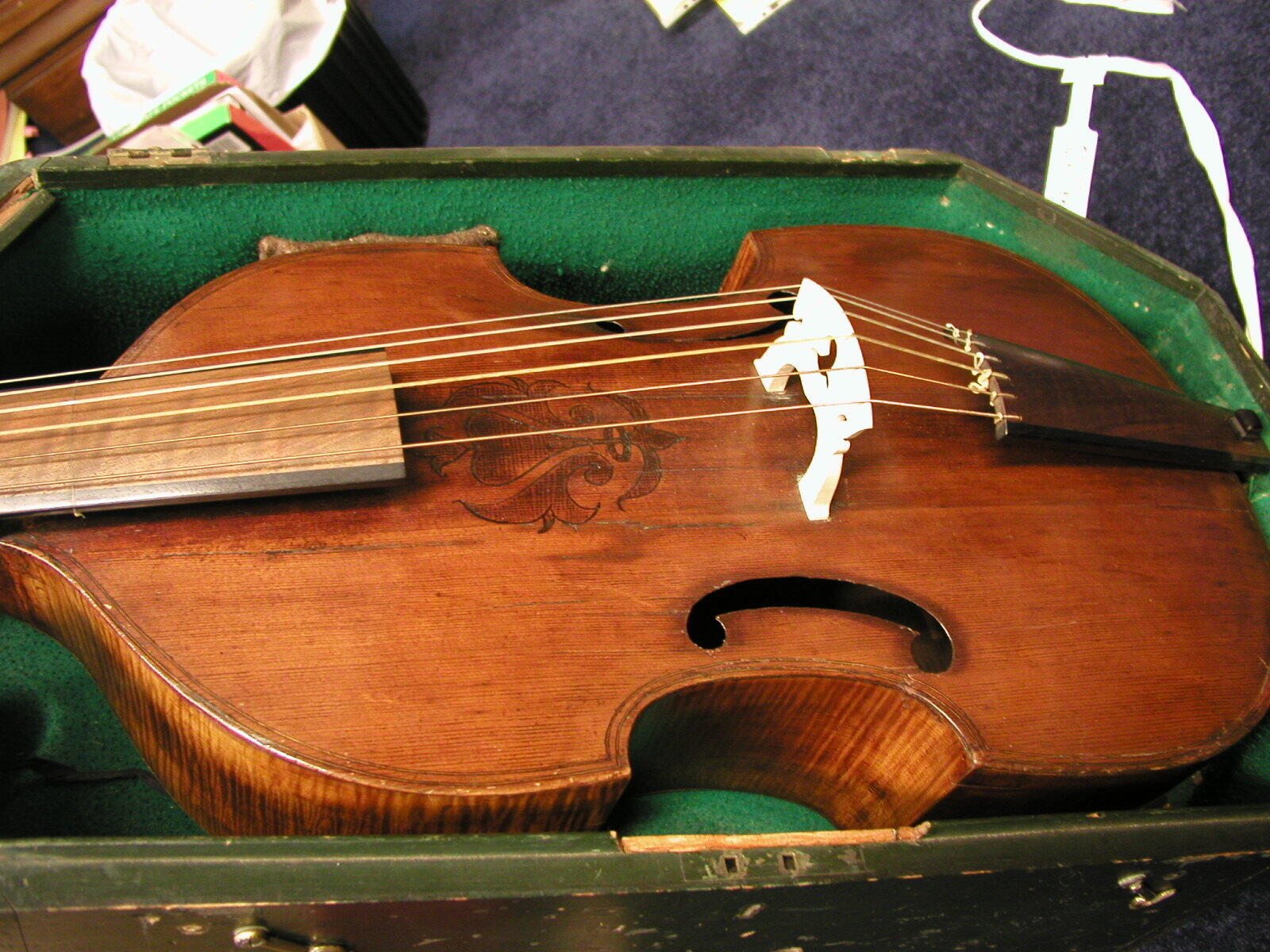 Un instrumento de cuerda antiguo con cuerpo de madera, intrincados tallados y cuerdas metálicas, guardado en un estuche forrado de verde.