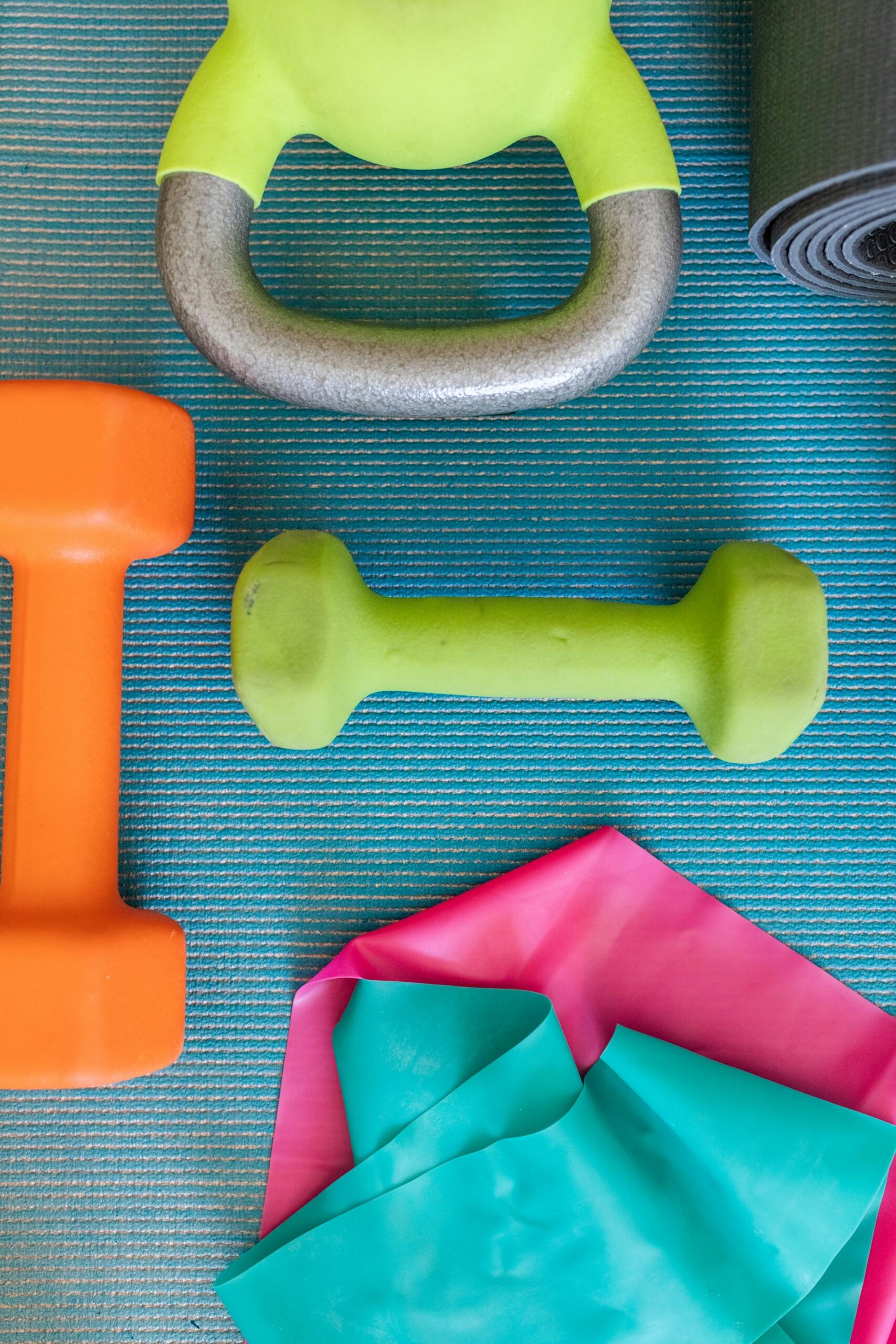 Equipos de fitness de colores sobre una colchoneta azul: kettlebell, mancuernas y bandas de resistencia.