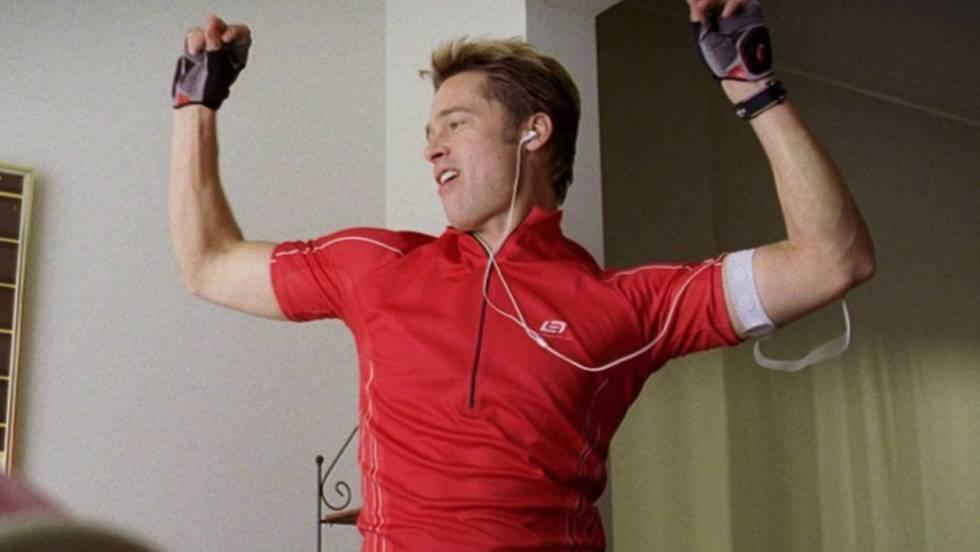 Hombre con camiseta roja deportiva celebrando mientras escucha música por sus auriculares.