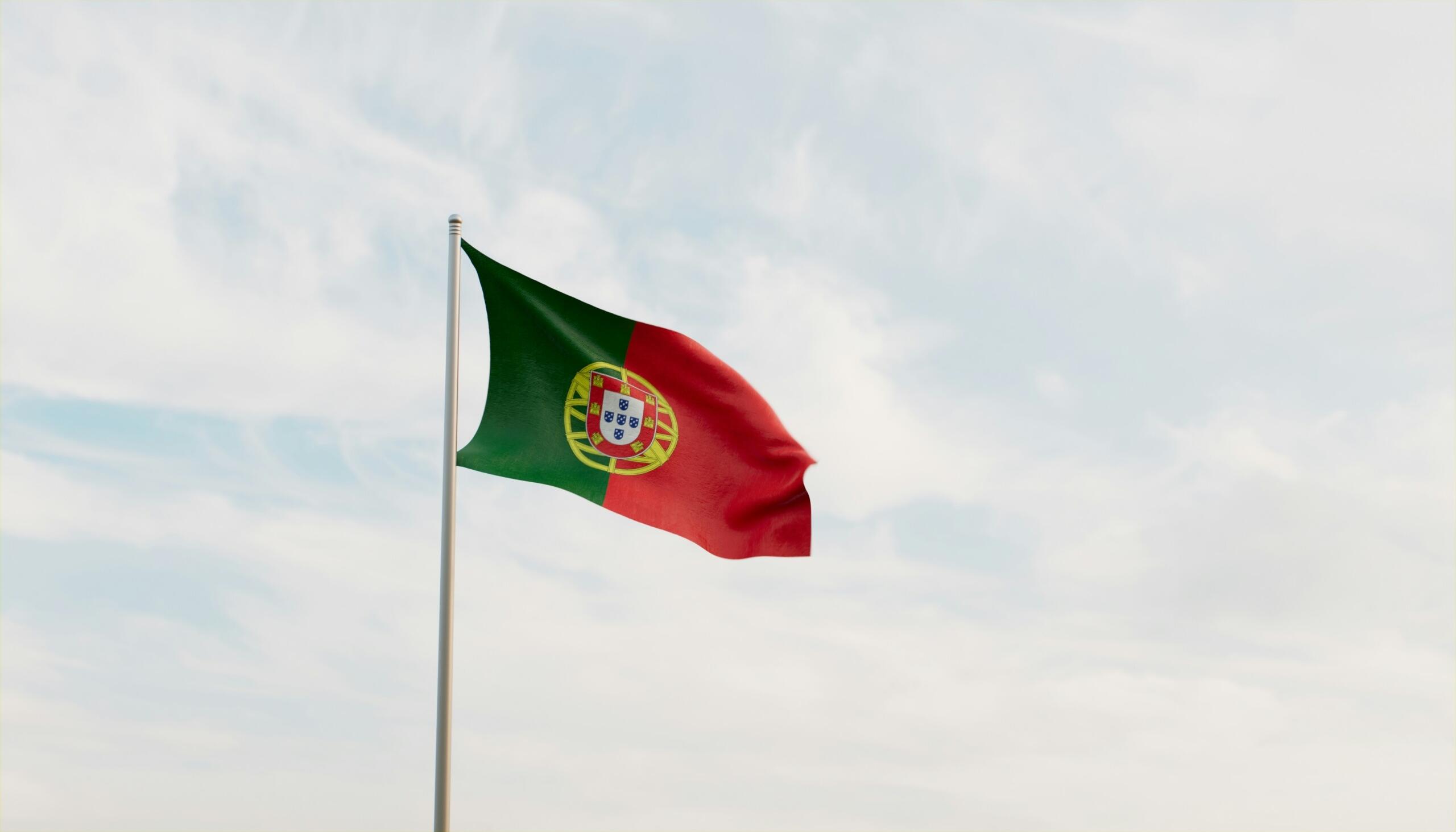 Bandera de Portugal ondeando contra un cielo nublado, con colores verde y rojo y el escudo nacional en el centro.