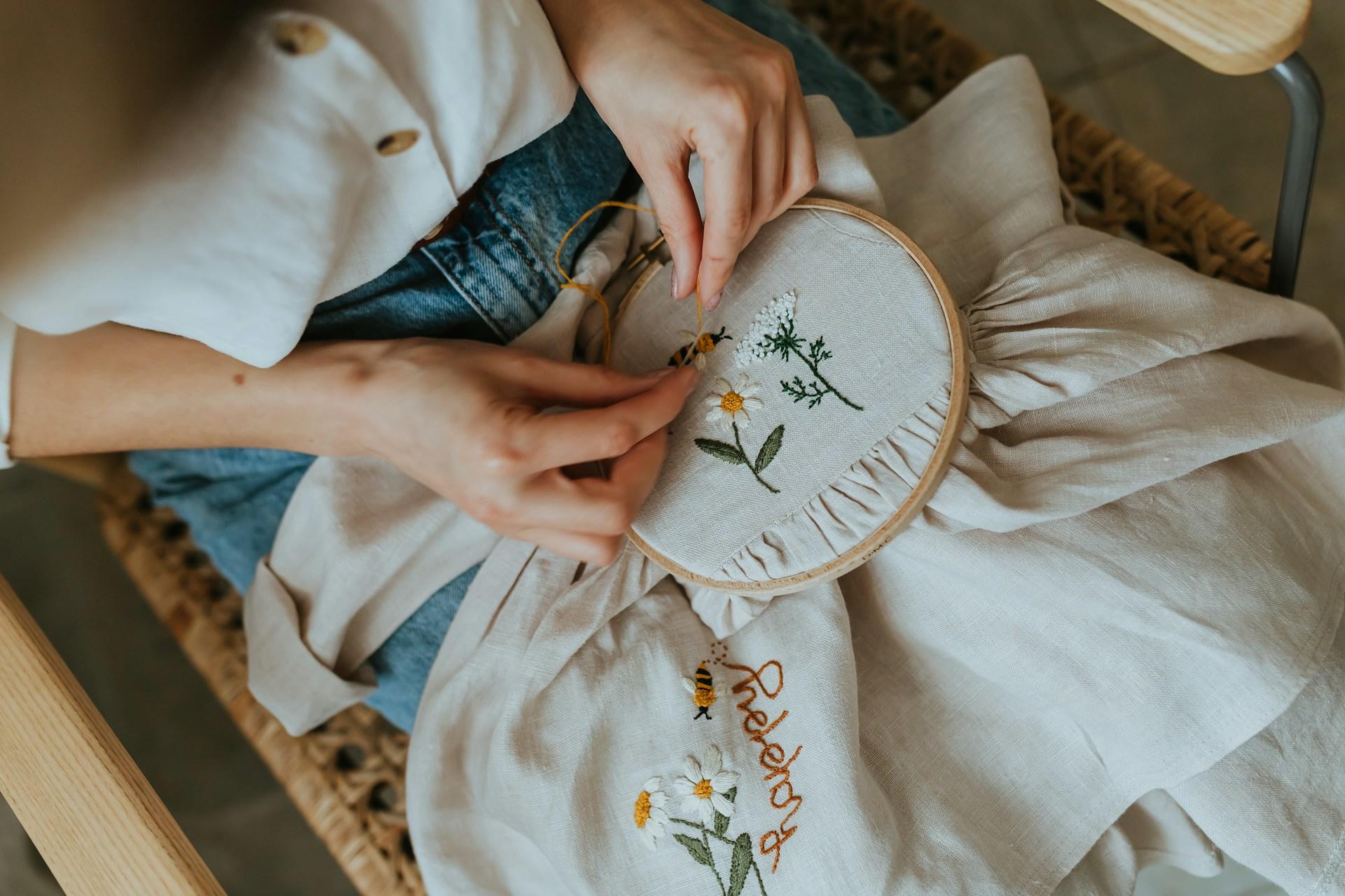 mujer bordando flores y abejas sobre una tela blanca